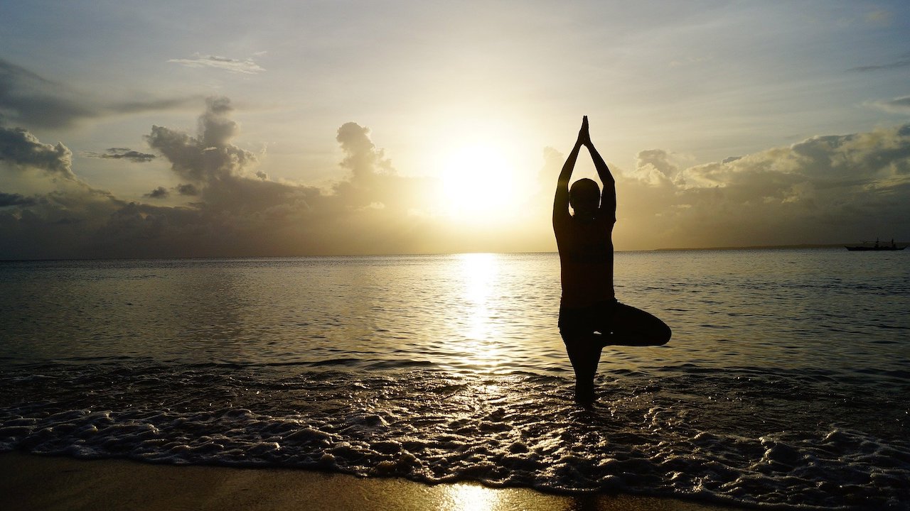 A person holding a yoga pose on a lake shore.