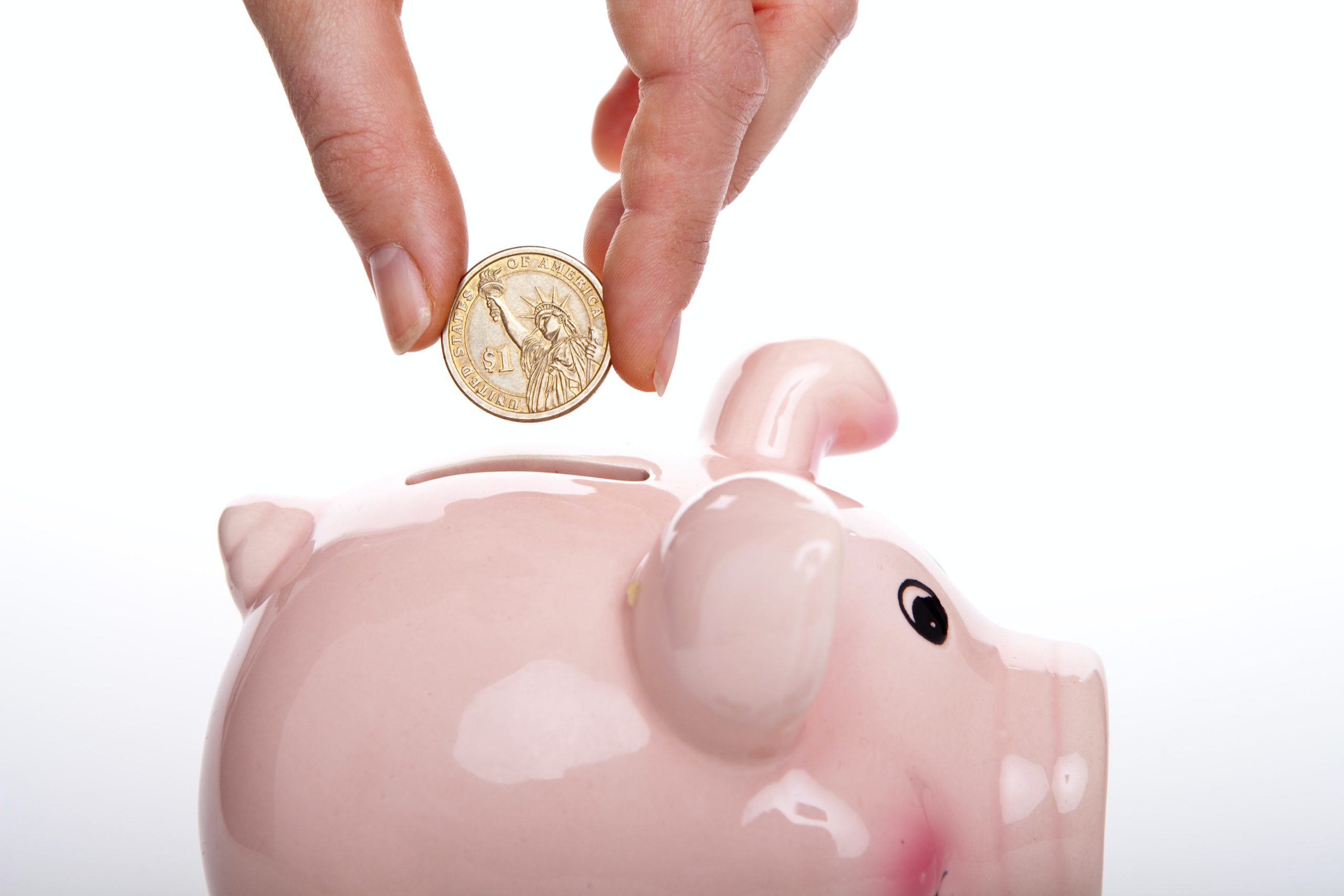 A hand putting a coin in a piggy bank.