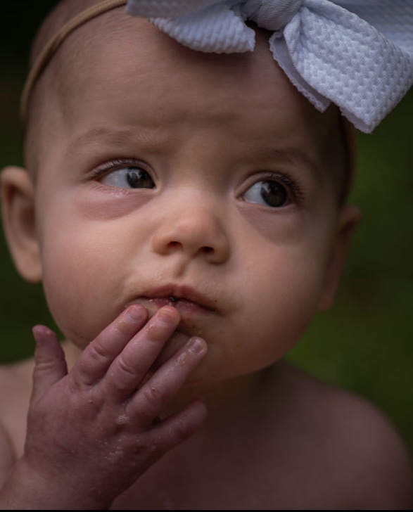 A baby with a hand on chin as if in thought. 