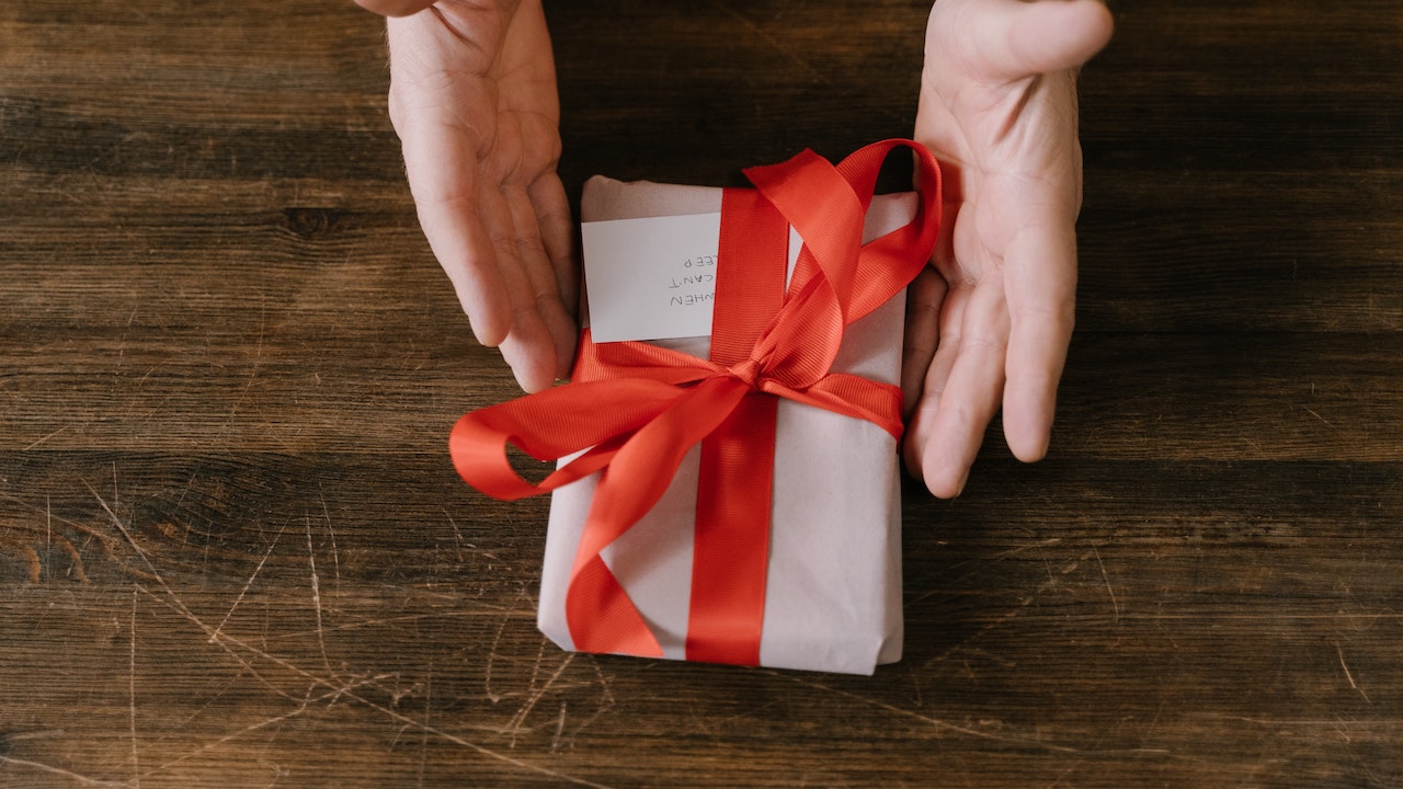 Hands proffering a small, gift wrapped package.